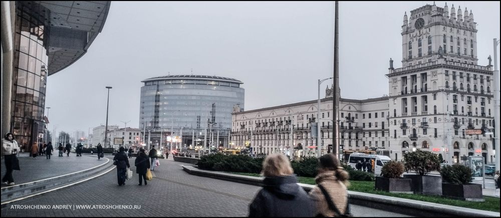 Комфортабельный автобус Ecolines на остановке в Минске на маршруте в Санкт-Петербург, вечерняя посадка пассажиров, вид на железнодорожный вокзал и архитектуру близ площади Бобруйской, начало романтического путешествия между Беларусью и культурной столицей России