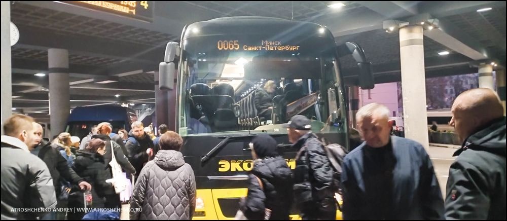 Комфортабельный автобус Ecolines на остановке в Минске на маршруте в Санкт-Петербург, вечерняя посадка пассажиров, вид на железнодорожный вокзал и архитектуру близ площади Бобруйской, начало романтического путешествия между Беларусью и культурной столицей России