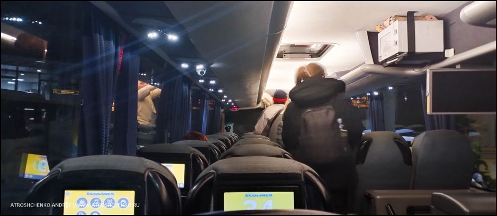 Комфортабельный автобус Ecolines на остановке в Минске на маршруте в Санкт-Петербург, вечерняя посадка пассажиров, вид на железнодорожный вокзал и архитектуру близ площади Бобруйской, начало романтического путешествия между Беларусью и культурной столицей России